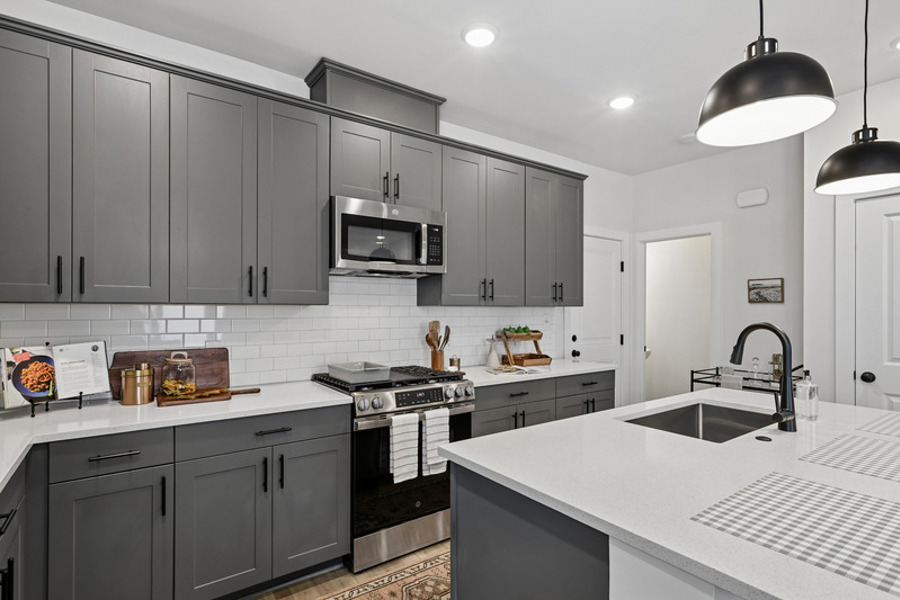 Modern townhome kitchen featuring quartz countertops, stainless steel appliances, gas range, white subway tile backsplash, and a large center island at HARMON West Meade in Nashville, Tennessee.