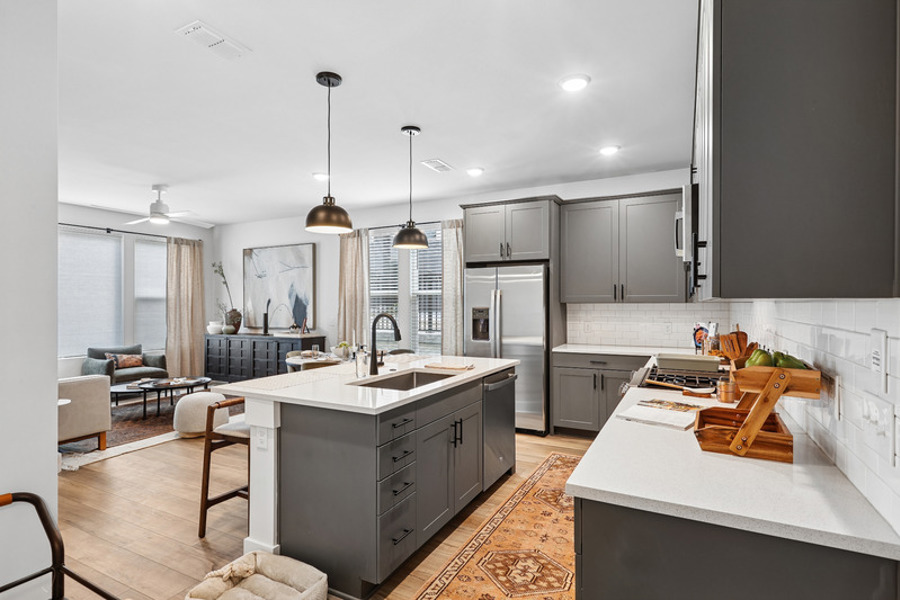 Open-concept townhome kitchen and living area featuring a large quartz island, stainless steel appliances, gas range, gray shaker cabinets, and contemporary finishes at HARMON West Meade in Nashville, Tennessee.