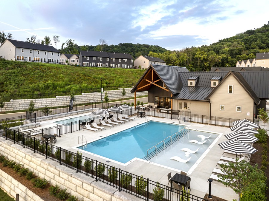 Resort-style swimming pool with tanning ledge, lounge chairs, striped umbrellas, and adjacent clubhouse at HARMON West Meade.