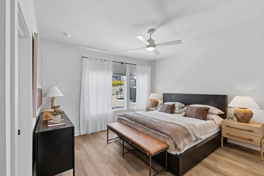 Spacious primary bedroom with modern finishes, wood-style flooring, ceiling fan, and large windows at HARMON West Meade in Nashville, Tennessee.